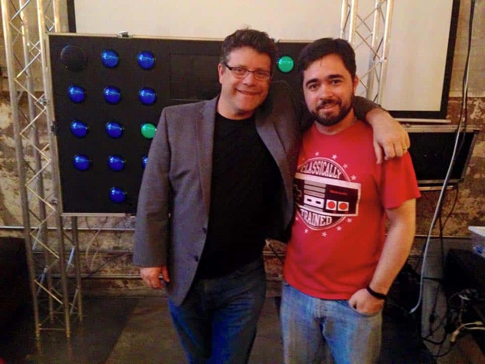 Two men smiling at a tech event, standing in front of a digital display.