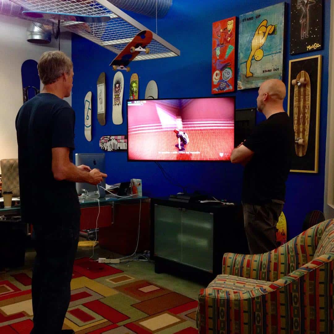 Two men viewing skateboard art display on a vibrant blue wall in a creative space.