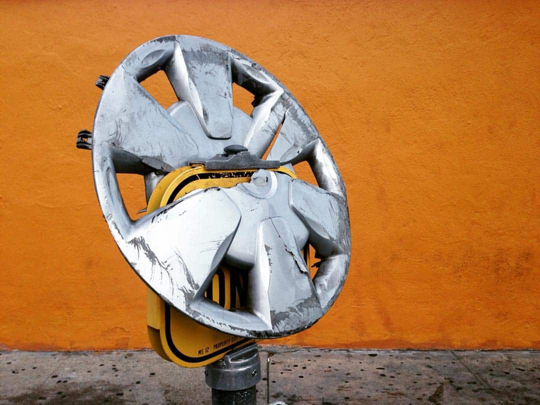 Wheelchair with a broken, scratched rim on a vibrant orange background.