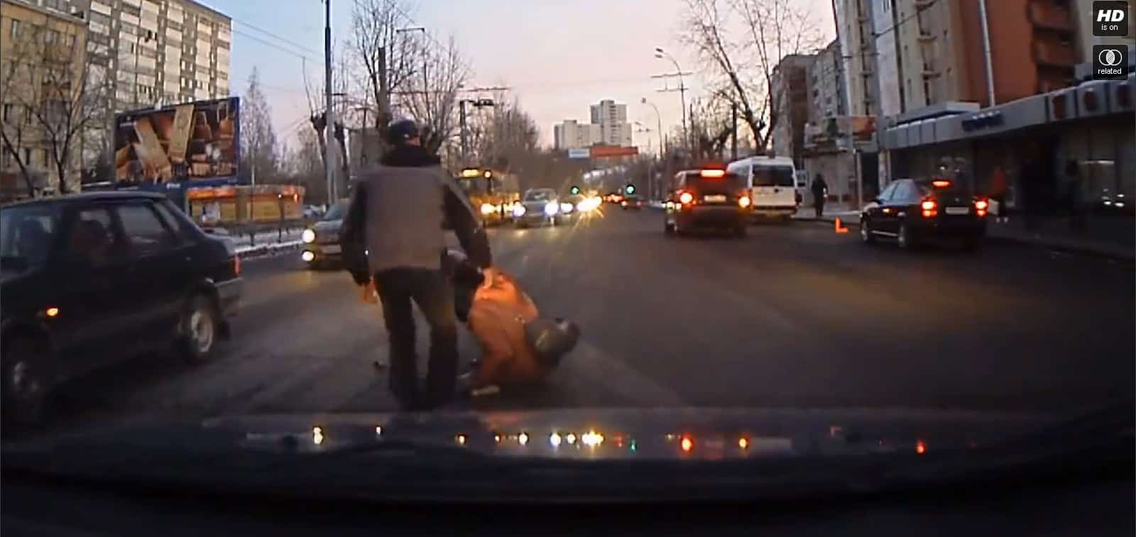 Pedestrian accident on city street with cars and a person lying on the road during evening hours.