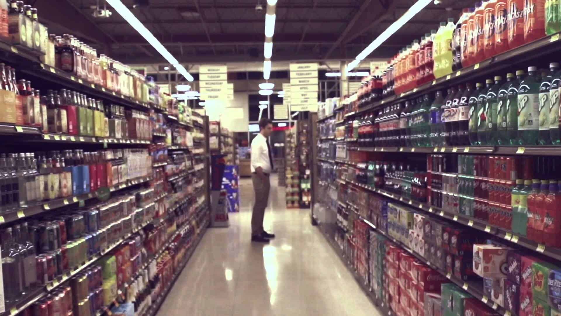 Aisle view of a grocery store with shelves filled with drinks and snacks on both sides.