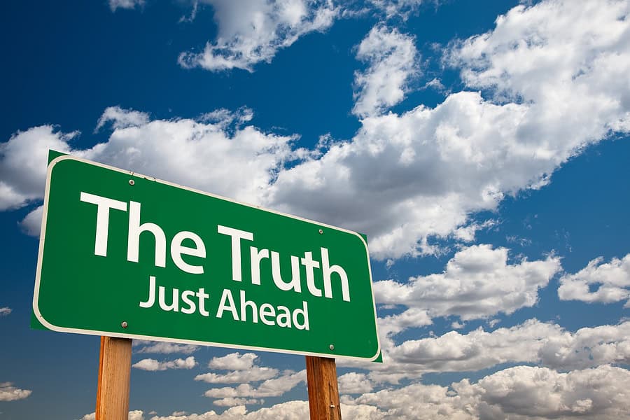 Green road sign reading "The Truth Just Ahead" against a cloudy sky background.