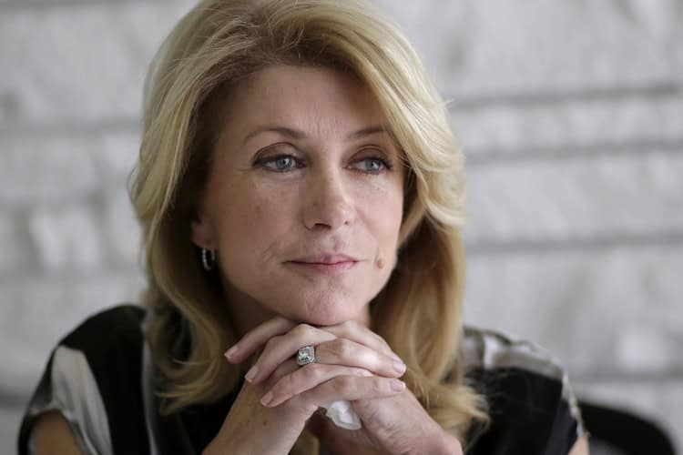 Thoughtful woman with blonde hair, gazing pensively, sitting indoors with a blurred background.