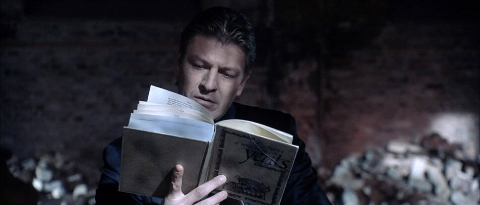 Man engrossed in reading a book in a dimly lit environment, focused on the content.